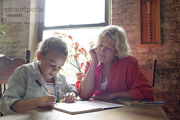 Frau sieht Enkelin bei den Hausaufgaben an  während sie am Tisch sitzt