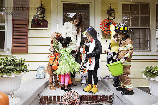 Frau verteilt Süßigkeiten an Kinder in Halloween-Kostümen während Trick oder Behandlung