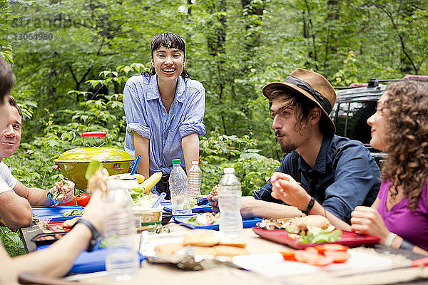 Frau schaut Freunde beim Essen am Picknicktisch im Wald