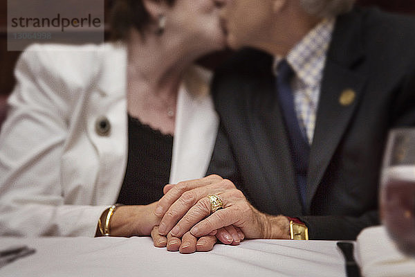 Mittelteil eines älteren Paares  das sich küsst  während es im Restaurant sitzt