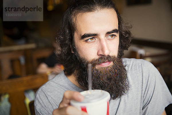 Nahaufnahme eines nachdenklichen Mannes mit Bart  der Cola trinkt  während er im Café sitzt