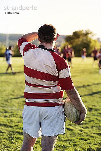Rückansicht eines Rugbyspielers  der den Ball hält  während er auf einem Rasenfeld steht
