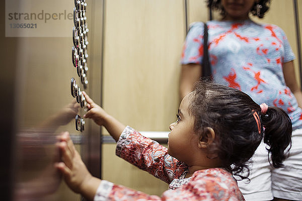 Mädchen drückt den Druckknopf  während es bei der Mutter im Aufzug steht