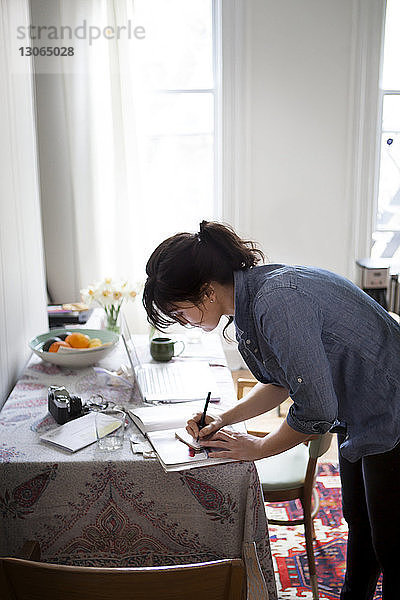 Seitenansicht einer Frau  die schreibt  während sie zu Hause am Tisch steht