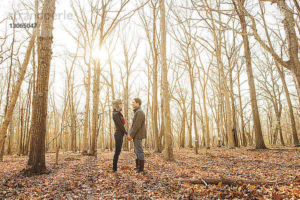 Seitenansicht eines im Wald stehenden Paares  das sich an den Händen hält