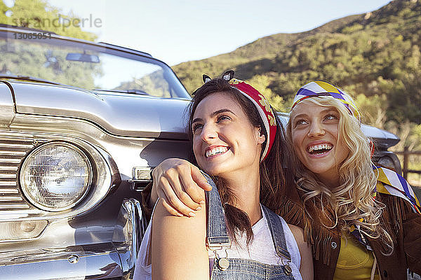 Glückliche Frauen schauen weg  während sie gegen ein Cabriolet sitzen