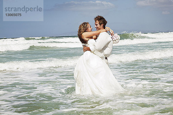 Im Meer stehendes Ehepaar am Strand gegen den Himmel
