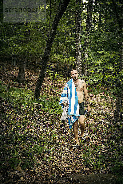 Mann ohne Hemd mit Handtuch und Kleidung beim Waldspaziergang