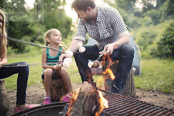 Vater und Tochter im Gespräch mit bratenden Marshmallows am Lagerfeuer