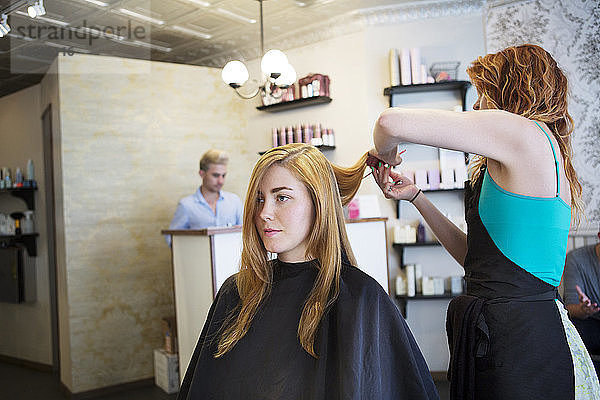Seitenansicht eines Friseurs  der die Haare der Frau im Salon schneidet