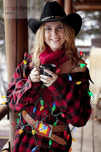 Porträt einer Frau mit Weihnachtsbeleuchtung auf der Veranda stehend