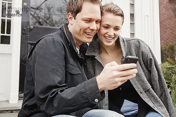 Ehepaar betrachtet Mobiltelefon  während es vor dem Haus sitzt