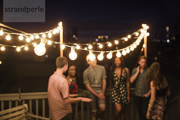 Freunde unterhalten sich  während sie nachts auf der Terrasse des Gebäudes am Geländer stehen