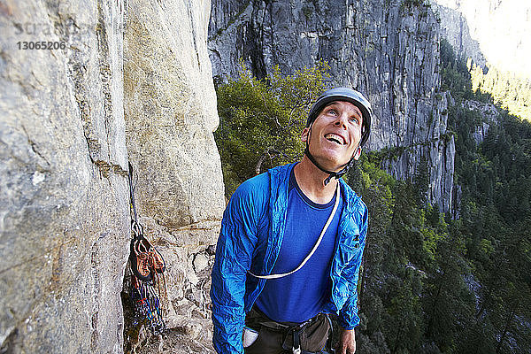 Glücklicher Mann schaut auf  während er an einer Felsformation gegen den Berg steht