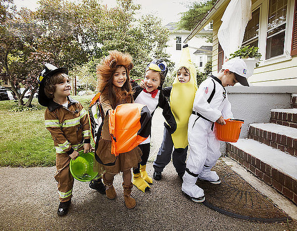 Glückliche Kinder in Halloween-Kostümen  die während eines Streichs oder einer Behandlung auf das Haus zugehen