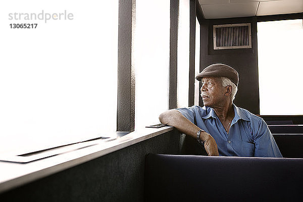 Nachdenklicher älterer Mann schaut durch Fenster  während er auf der Fähre reist