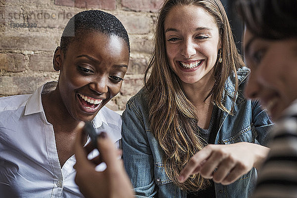 Frau zeigt Freunden ihr Smartphone  während sie im Café sitzt
