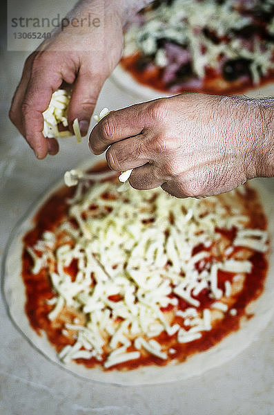 Draufsicht auf Hände  die Käse auf rohe Pizza legen