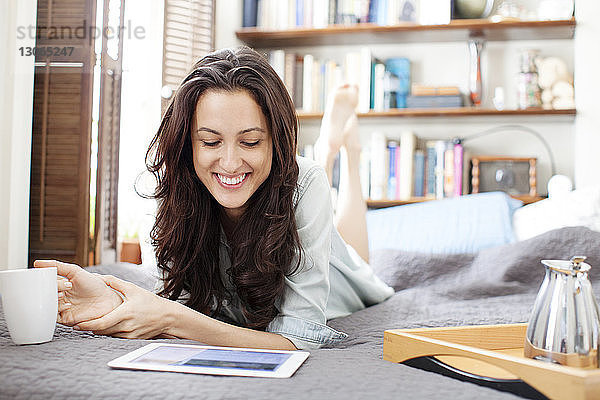 Glückliche Frau schaut auf Tablet-Computer  während sie auf dem Bett liegt