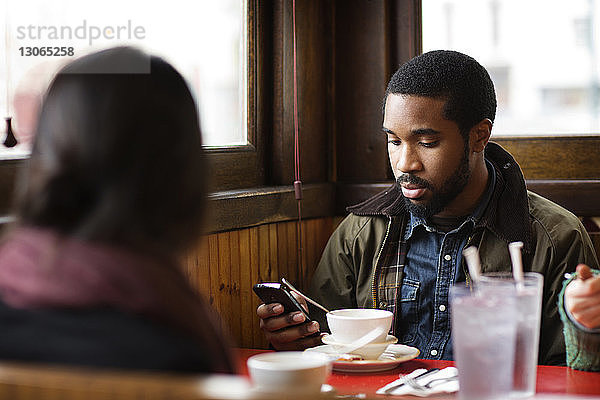 Mann benutzt Smartphone  während er mit Freunden im Restaurant sitzt