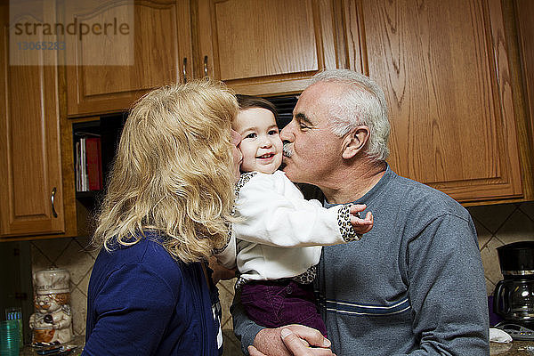 Großeltern küssen Kind  während sie in der Küche stehen