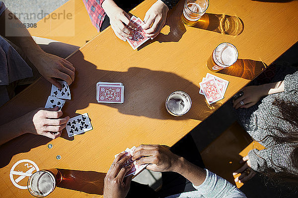 Ausgeschnittenes Bild von Freunden beim Kartenspielen bei Bier am Tisch in einer Brauerei