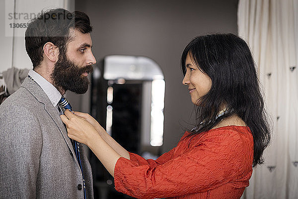Lächelnde Frau passt Krawatte am Ehemann zu Hause an