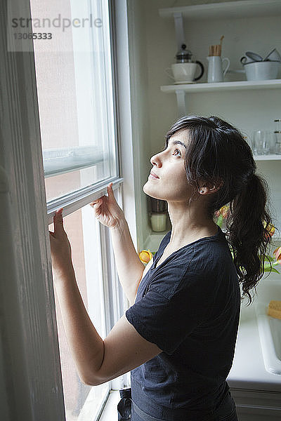 Seitenansicht der Frau beim Öffnen des Fensters zu Hause