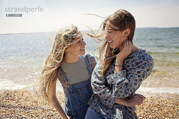 Fröhliche Freunde unterhalten sich im Stehen am Strand