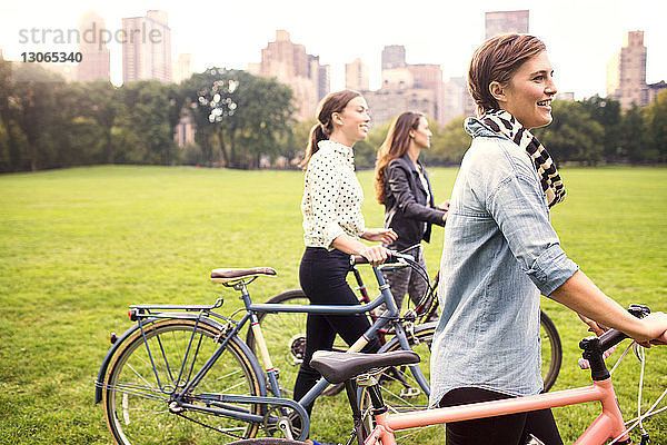 Frauen mit Fahrrädern gehen auf dem Feld im Park gegen die Stadt