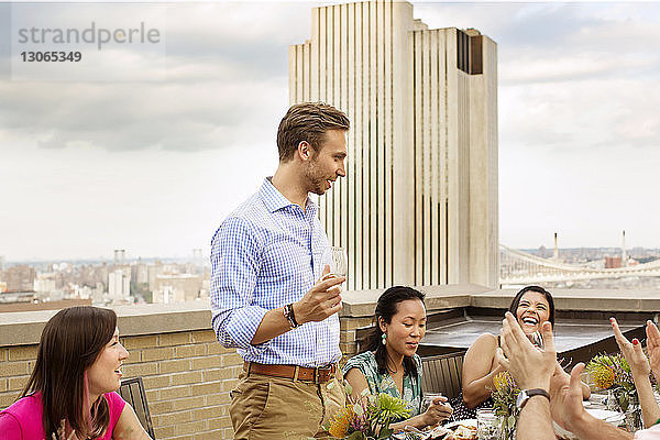 Glückliche Freunde sehen einen Mann  der bei Tisch mit Wein anstößt  auf dem Gebäude Terrasse gegen den Himmel