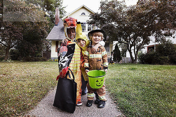 Porträt von lächelnden Freunden in Halloween-Kostüm  die während eines Streichs oder einer Behandlung vor dem Haus stehen