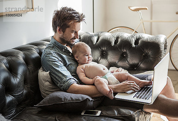 Glücklicher Mann benutzt Laptop-Computer  während er mit seinem Sohn zu Hause sitzt