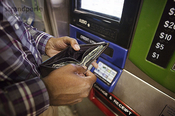 Hochwinkelansicht eines Mannes  der eine Brieftasche hält  während er gegen einen Geldautomaten steht