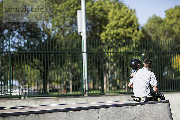 Rückansicht von Vater und Sohn im Skateboard-Park sitzend