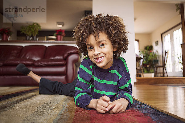 Porträt eines glücklichen Jungen  der zu Hause auf dem Teppich liegt