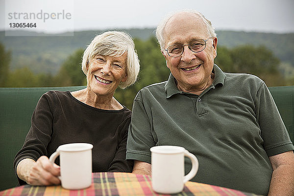 Porträt eines lächelnden älteren Ehepaares  das am Tisch auf dem Rasen sitzt