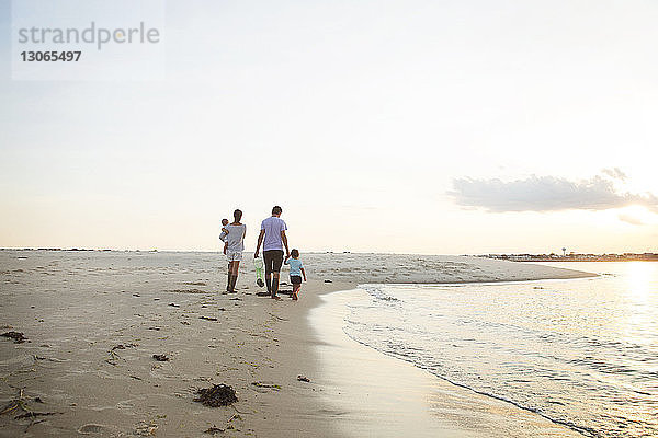 Rückansicht von Eltern  die mit Kindern am Strand spazieren gehen  gegen den Himmel