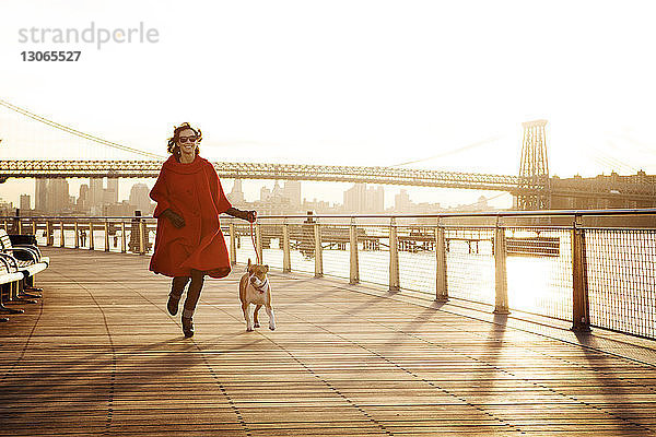 Frau rennt mit Hund auf der Promenade gegen die Williamsburg-Brücke