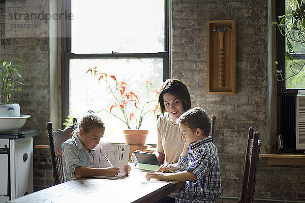 Mutter hilft Kindern bei den Hausaufgaben  während sie am Tisch sitzen