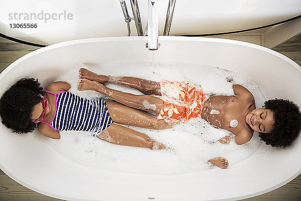 Draufsicht auf verspielte Geschwister  die in der Badewanne liegen