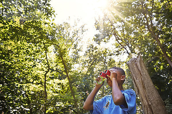 Junge schaut durch ein Fernglas im Wald