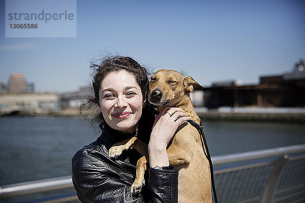 Porträt einer glücklichen Frau mit Hund auf einem Steg gegen den Himmel stehend