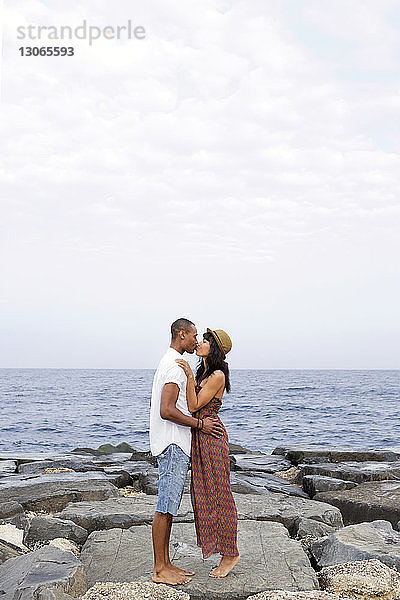 Seitenansicht eines Paares  das sich küsst  während es auf Felsen am Strand steht