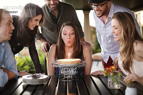 Frau bläst während der Geburtstagsfeier auf der Veranda mit Freunden Kerzen aus