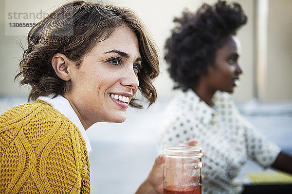 Lächelnde Frau hält Trinkglas in der Hand  während ihr Freund im Hintergrund sitzt