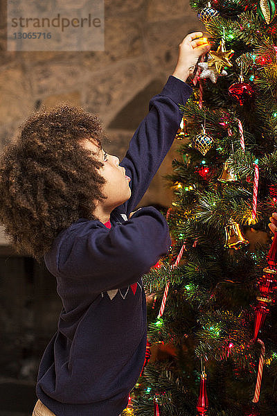 Seitenansicht eines Jungen  der zu Hause den Weihnachtsbaum schmückt