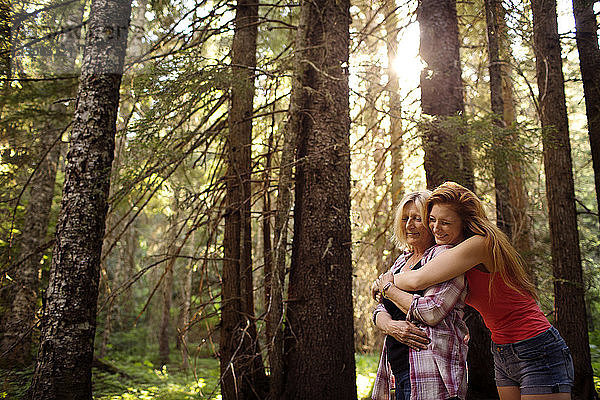 Glückliche Mutter und Tochter umarmen sich  während sie inmitten von Bäumen im Wald stehen