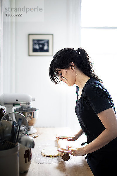 Seitenansicht einer Frau  die bei der Arbeit in der Küche Teig rollt