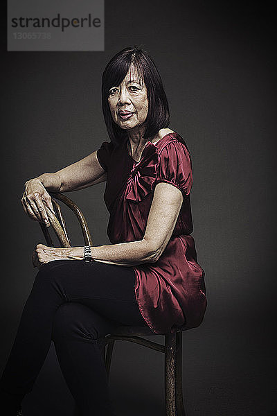 Porträt einer älteren Frau  die auf einem Stuhl vor schwarzem Hintergrund sitzt